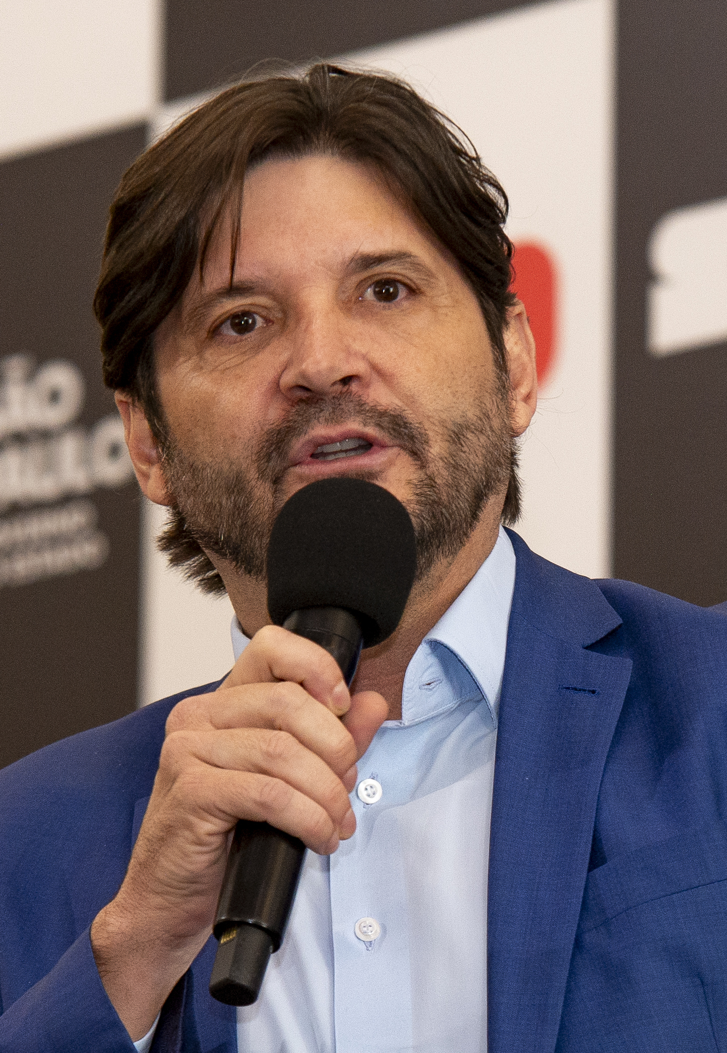 André do Prado, de terno azul, fala ao microfone durante evento